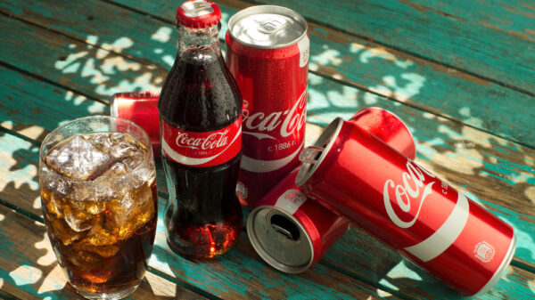 glass of Coca-Cola with ice, can and bottle of Coca-Cola on wooden background.