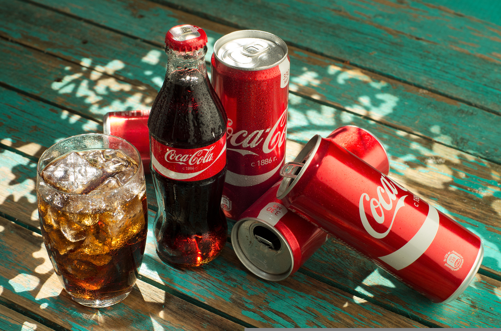 glass of Coca-Cola with ice, can and bottle of Coca-Cola on wooden background.