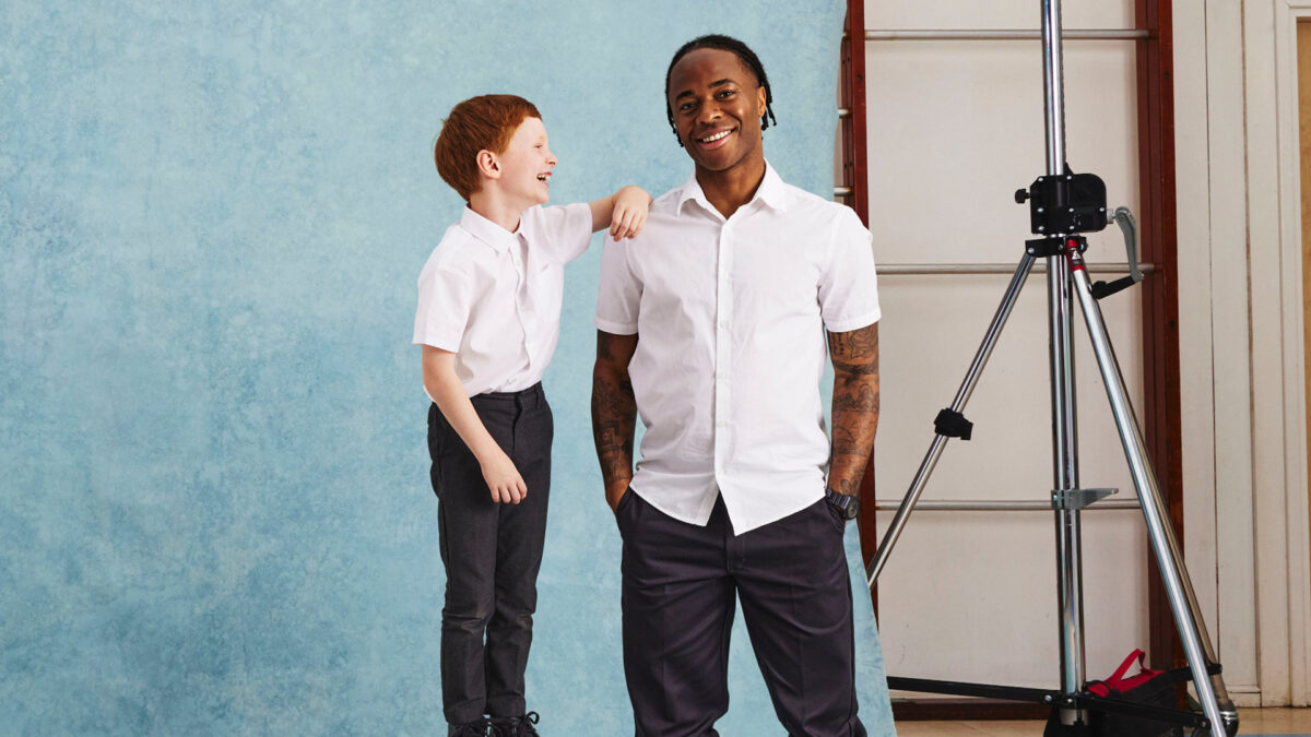 Raheem Sterling with child, both smiling at the camera and in 'Back to School' styled clothes.
