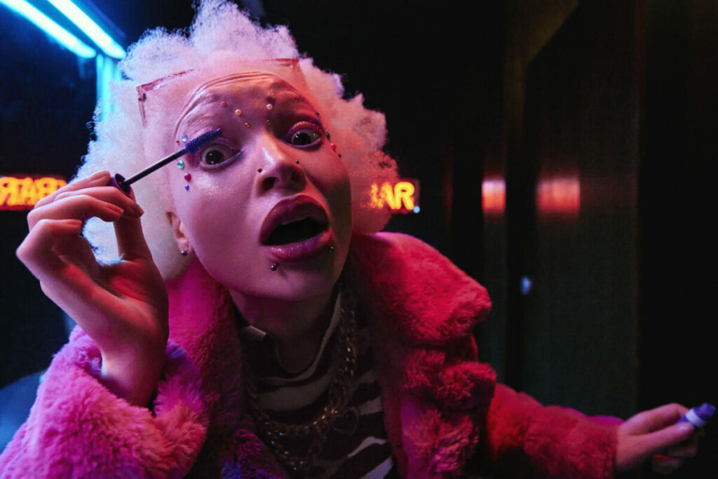 A still from the RNIB campaign - showing a person in a pink coat, white hair in a dark room applying mascara.