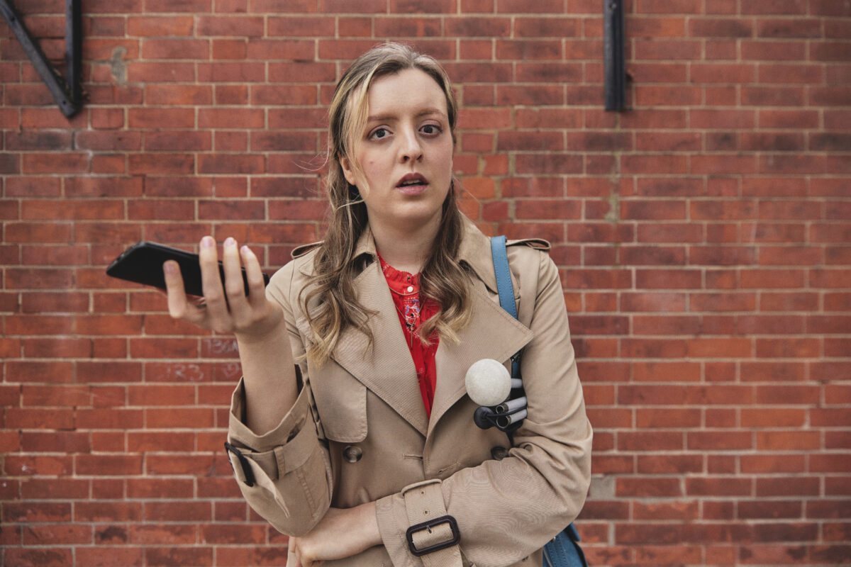 A still from RNIB shows a visually impaired person from the film in a beige trench boat holding a phone - against a brick background