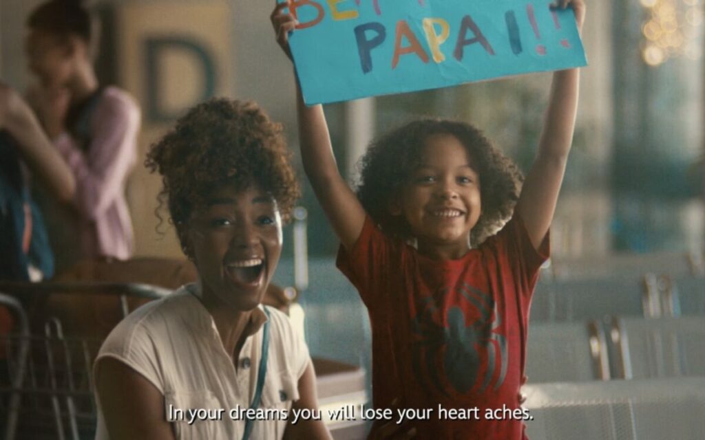 Disney has launched a live-action holiday campaign, 'May Your Wishes Comes True', focusing on the power of wishes for its 100th anniversary, here depicting a mother and a son in the airport. The mother is crouched down to her son's height and is singing while the young boy raises a sign.