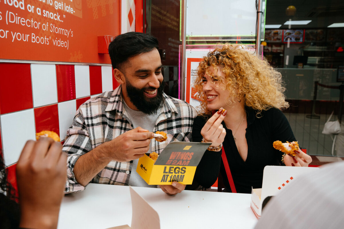 Gymbox Morleys collab, people eating out of Gymbox chicken boxes. Gymbox will partner with the high street classic chicken shop Morley's as it brings its latest OOH campaign to life, in a bid to show how the gym embraces Londoner's through every aspect of their lifestyle.