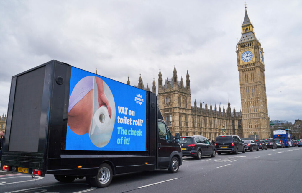 Image of Who Gives A Crap van in front of Parliament reading "VAT on toilet roll? The cheek of it?2 accompanied by an image of someone holding toilet roll in their knickers. Who Gives A Crap urges gov to "scrap the roll tax" in fresh stunt