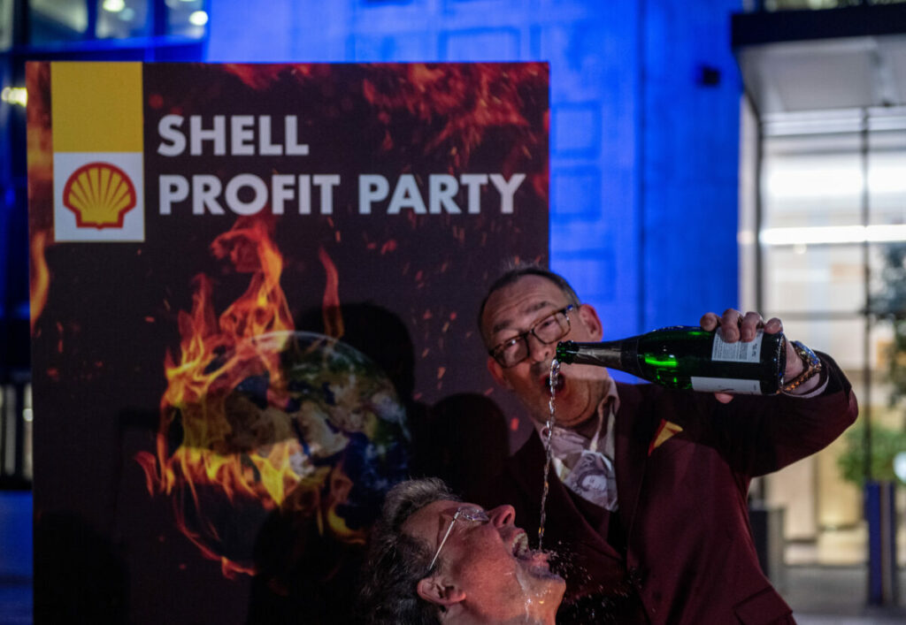 Greenpeace activists disguised as Shell executives drink champagne and dance around a burning sign reading ‘Your Future’ at a mock party outside the Shell