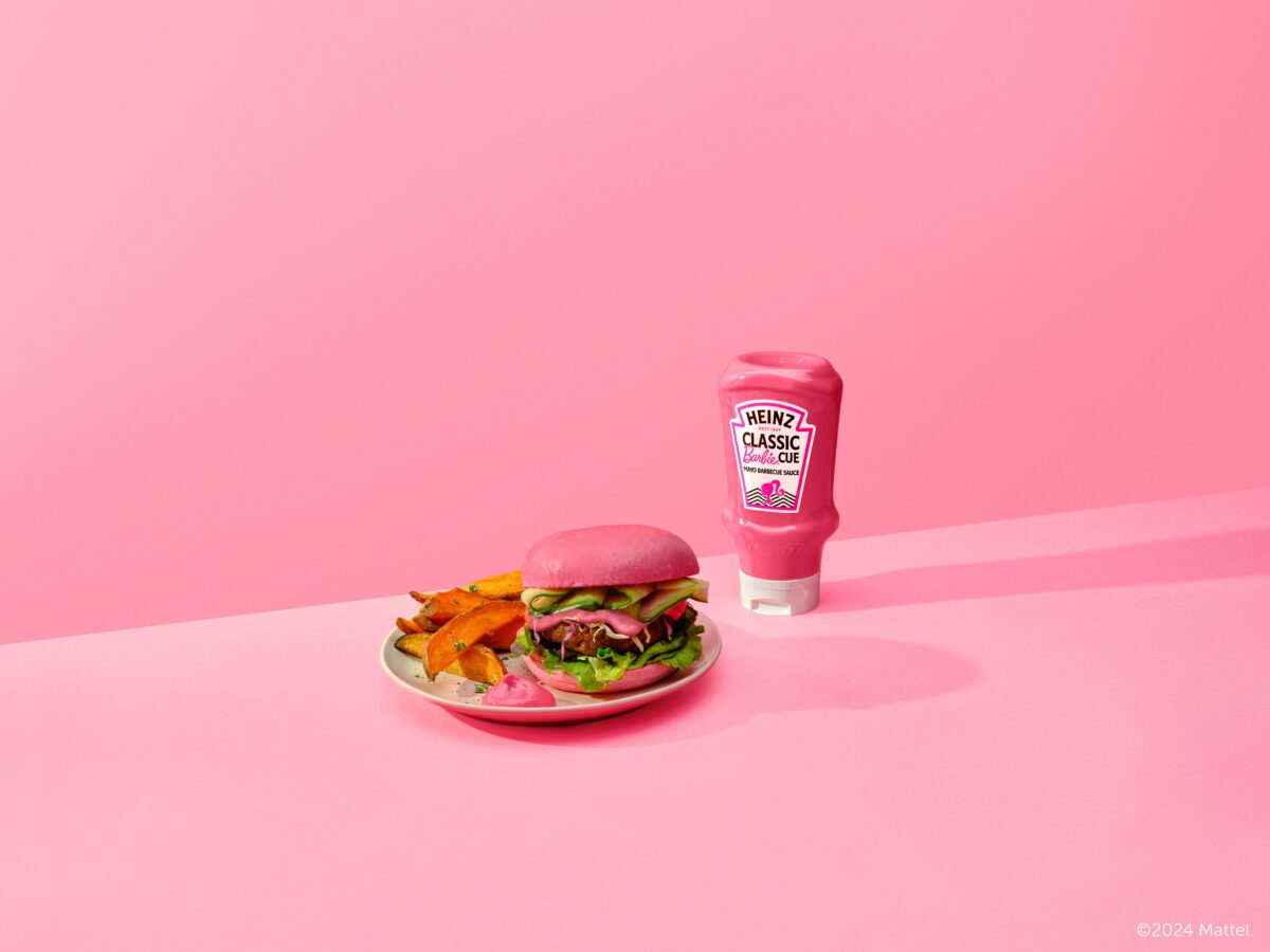 The pink coloured Barbie cue sauce in the traditional Heinz bottle is shown with a Barbie logo on it and a modern image of a woman in a pony tail and then a modern style pattern next to it. To the side of the bottle is a burger and some sweet potato. Their is a dollop of the sauce on the plate next to the burger. The background is Barbie pink, tying it in with the doll's brand.