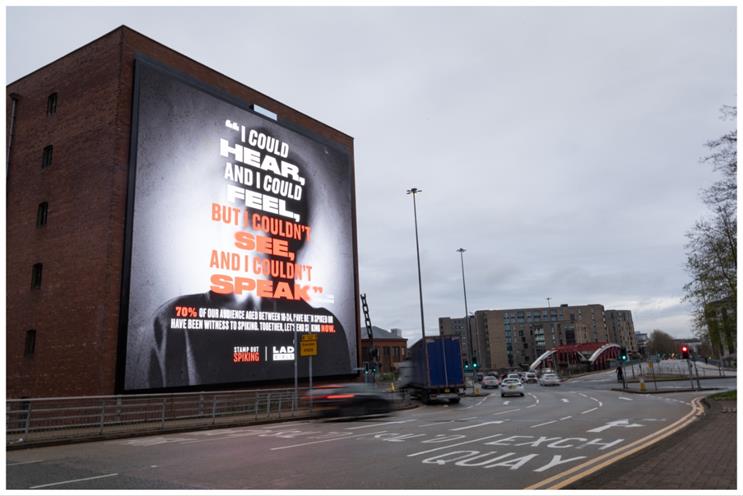 A roadside billboard with a dark background and a shadowy figure blurred to stop people identifying them reads "I could hear, and I could feel, but I couldn't see, and I couldn't speak". Underneath the text the statistic that 70% of 17-24 year olds have experienced or been witness to spiking. Underneath are the logos for Stamp Out Spiking and the youth-focused magazine LadBible.