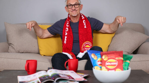 Crisp brand Walkers is giving football fans the chance to watch the sold out UEFA Champion's League final in a VIP box at Wembley with Gary Lineker. The image shows Gary Lineker sat at home on a sofa with a Walkers scarf around his neck. He is smiling, surround by magazines cups of tea and of course a bowl of Walkers.