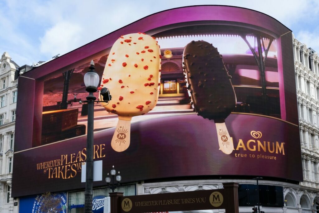 Magnum has launched a new 3D OOH billboard in iconic locations across the UK, including Piccadilly Lights, in order to celebrate this year's new flavour innovations Euphoria and Chill. Image shows a giant billboard with two magnum flavours the pink lemondade euphoria one and magnum's "chill" blueberry cookies flabour which is chocolate. The billboard marks part of the largest campaign in the UK.