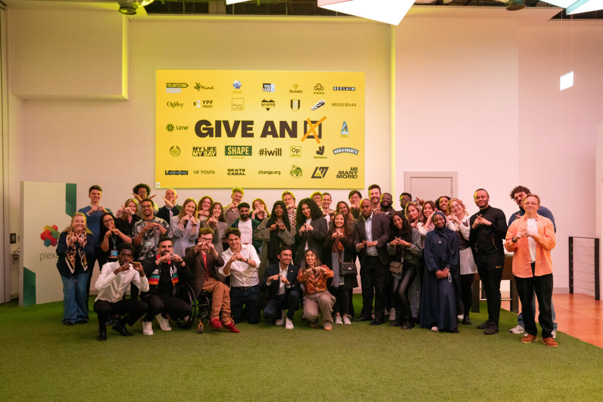 Members of the Give an X campaign team and partners all pose, smiling and making an X with their fingers.