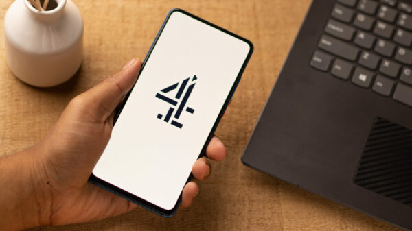 A person holds a phone ready to access Channel 4 content, a 4 on the phone screen as it loads up. There is also a candle and a computer in shot. Channel 4 has trebled viewings of TV shows on YouTube and digital-first hits on Channel 4.0, according to its latest update.