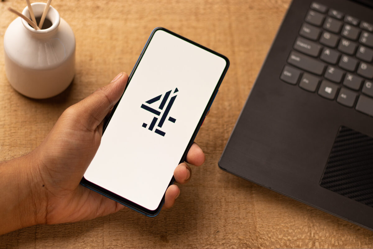 A person holds a phone ready to access Channel 4 content, a 4 on the phone screen as it loads up. There is also a candle and a computer in shot. Channel 4 has trebled viewings of TV shows on YouTube and digital-first hits on Channel 4.0, according to its latest update.