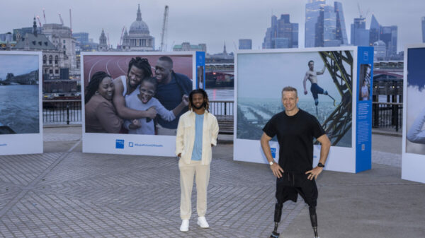 Emmanuel Oyinbo-Cocker and Richard Whitehead MBE stand in front of their portraits by Annie Leibovitz. Oyinbo-Cocker has a summery suit on. Richard Whitehead MBE stands hands on hisps, both are smiling. Creative communications agency Pretty Green and healthcare firm Bupa have tapped Annie Liebowitz for a health campaign that showcases what healthcare means to Paralympic athletes.