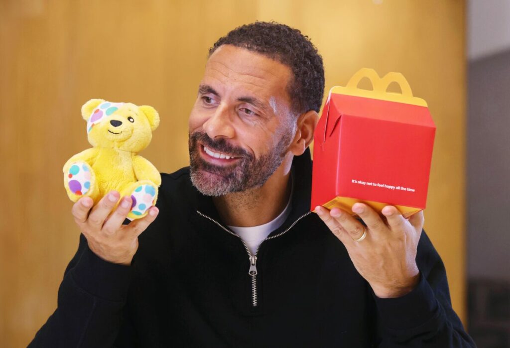 Rio Ferdinand holds up a Pudsey Children In Need toy and one of the new Happy meal boxes which has the happy smile removed and has text reading "It's ok not to feel happy all the time". McDonald's has removed the happy smile from its happy meal boxes for the first time, effort to encourage family conversations about mental health fronted by Manchester United legend Rio Ferdinand.