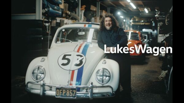 A long haired man stands in front of a retro Volkswagen white with a racing number 53 on the front, looking classic. Luke has long hair , and is relaxed resting on the side of the car. Text reads Lukes Wagen. Volkswagen is celebrating its heritage as "the people's car" in a new brand platform tapping into real-life VW stories and emotional connections.