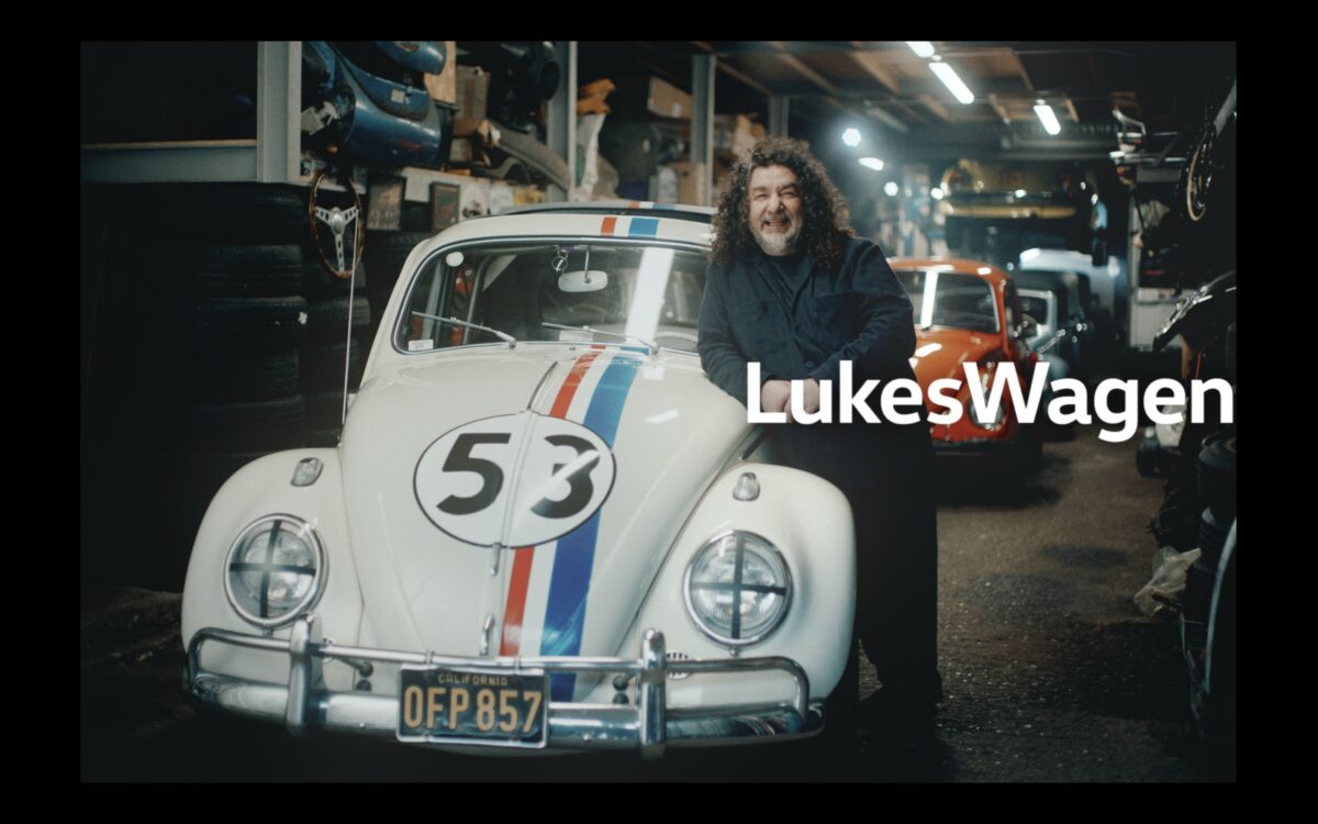 A long haired man stands in front of a retro Volkswagen white with a racing number 53 on the front, looking classic. Luke has long hair , and is relaxed resting on the side of the car. Text reads Lukes Wagen. Volkswagen is celebrating its heritage as "the people's car" in a new brand platform tapping into real-life VW stories and emotional connections.