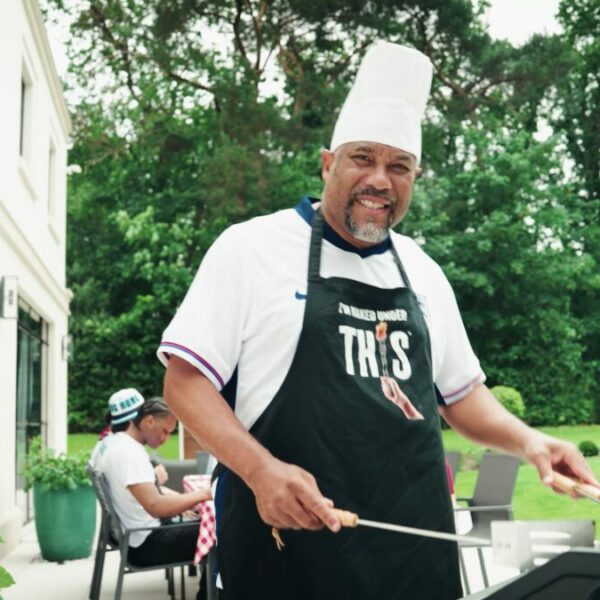John Barnes, clad in chefs gear, at thr barbecue. Footballing legend John Barnes has teamed up with plant-based food firm This to launch a new summer BBQ banger ahead of the Euros.