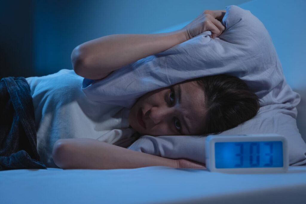 Woman kept awake by alarm. Alarm reads 3 am. She squashes her head in the pillow. CIM study reveals marketers are tossing and turning due to a range of issues, with over half fearing burnout due to the industry's culture (56%), according to new research from the Chartered Institute of Marketers (CIM).