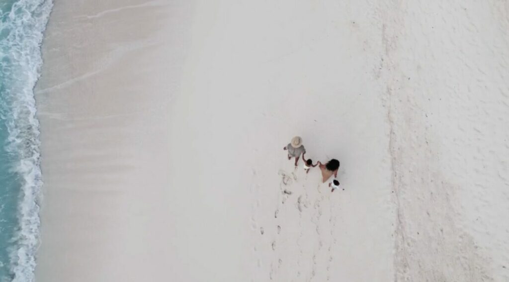 An arial shot of a family hand in hand walking across thhe golden sand.