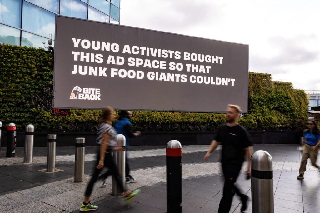 New Bite Back billboard at Westfield reads "Young activists bought this ad space so that junk food giants couldn't. Youth activists from Bite Back hijacked billboard space at Westfield White City as part of an anti-junk food campaign about HFSS foods.