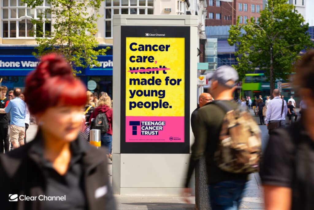 A bllboard features the text Cancer care wasn't made for young people. in black bold text against a yellow background. Bright pink corrections change the phrase into "Cancer care, wasn't made for young people." Teenage Cancer Trust's newest campaign shows the need for cancer care that caters to teenagers better, and how it contributes to the solution.