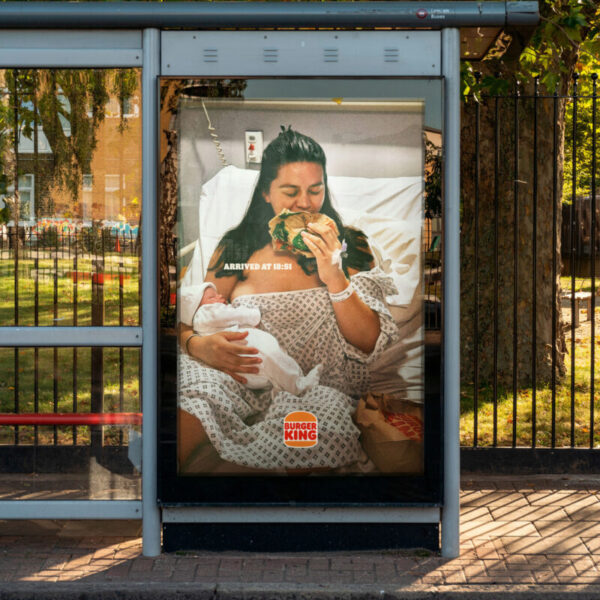 A new mum holding her sleeping new-born baby wearing a hospital gown munches ravenously on a Burger King burger.