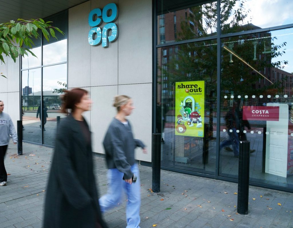 Two passers by walking past a Co-op store. Co-op will take the number of digital screens across its stores to over 9,000. The new screens will appear in busy urban areas to maximise reach.