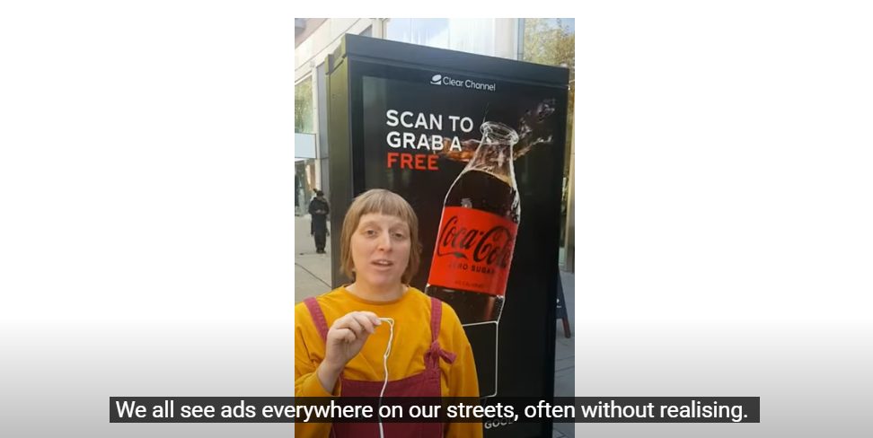 A woman dressed in a yellow jumper and dungarees talks through the project. AdFree Cities has started a new projected which encourages families to catalogue the billbaords they see on the way to school.