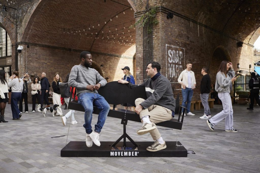 Two men on the see-saw like bench in Borough Yard. Men's health charity Movember created a moustache-shaped bench to engage more men in conversations with one another ahead of Movember.