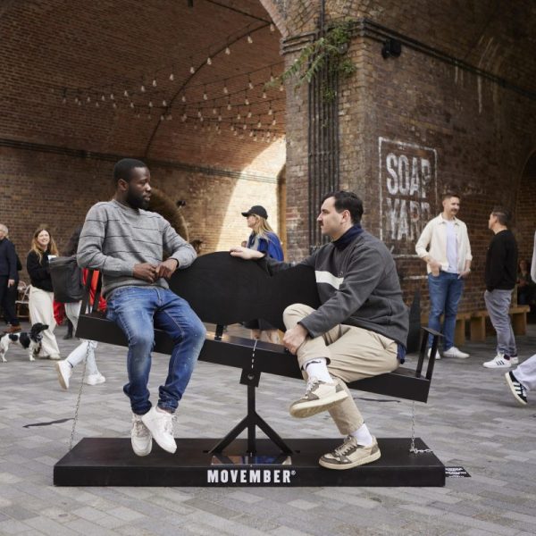 Two men on the see-saw like bench in Borough Yard. Men's health charity Movember created a moustache-shaped bench to engage more men in conversations with one another ahead of Movember.